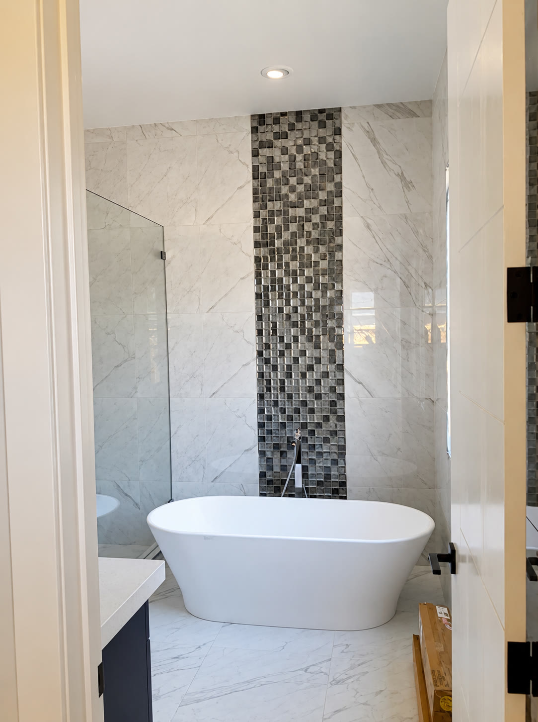 Freestanding bathtub with marble-look tile and mosaic feature wall