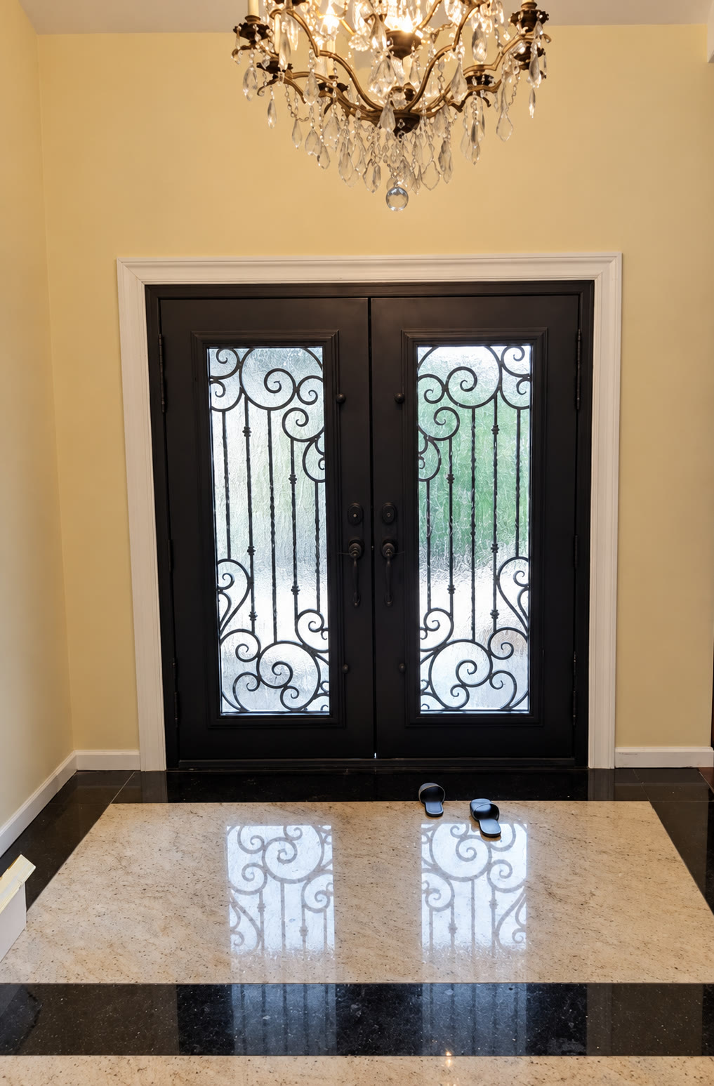 Decorative double entry doors below a crystal chandelier